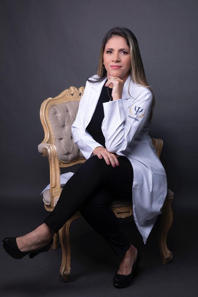Mirthes Oliveira sentada em uma poltrona, de jaleco